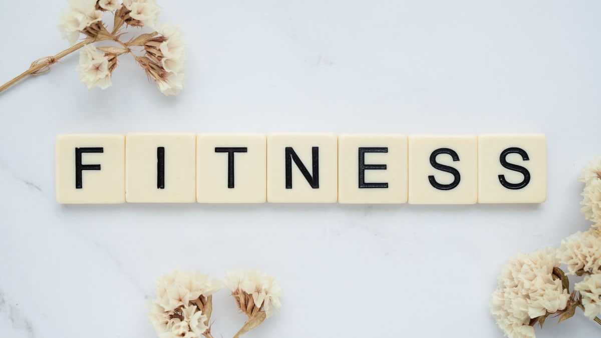 Close-up of scrabble tiles spelling 'FITNESS' on a marble surface with white flowers.
