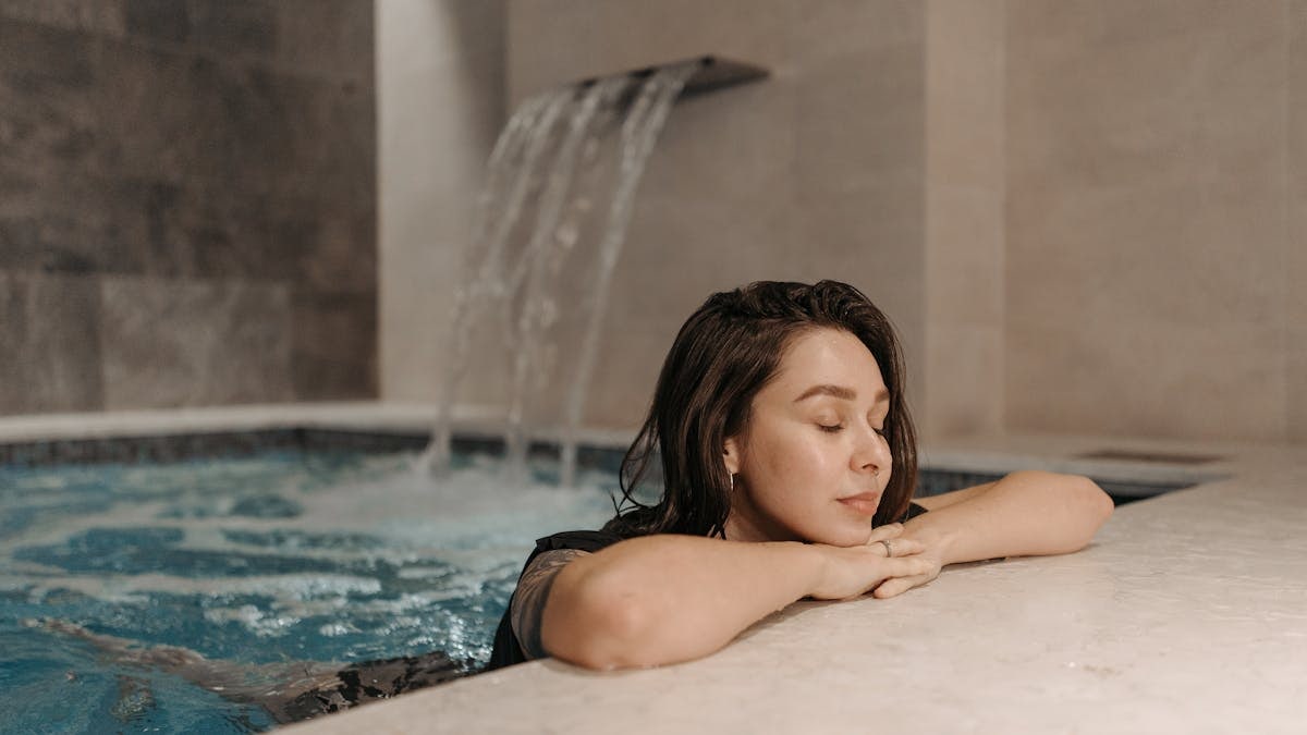 Caucasian woman enjoying a calm moment in an indoor swimming pool spa setting.